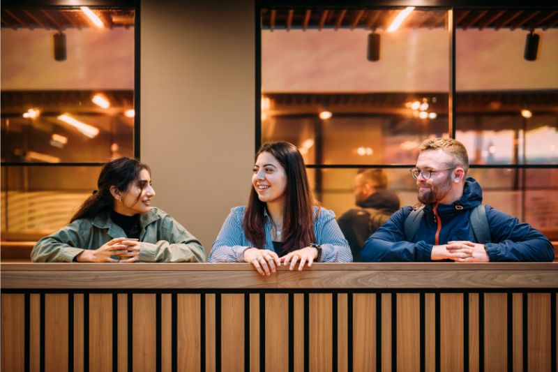 three students standing chatting over balcony